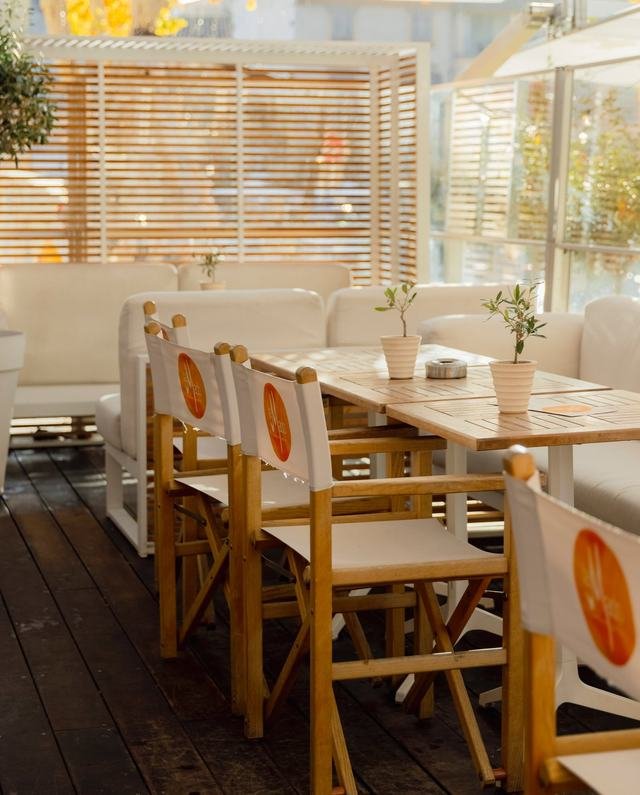 La terrasse de La Mado : tables en bois, chaises metteur en scène blanches au logo orange et oliviers en pot, place des Prêcheurs à Aix-en-Provence.